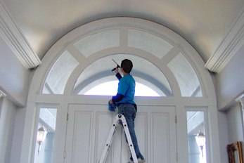 Valley Window & Gutter Cleaning technician on a ladder cleaning an arched entry window