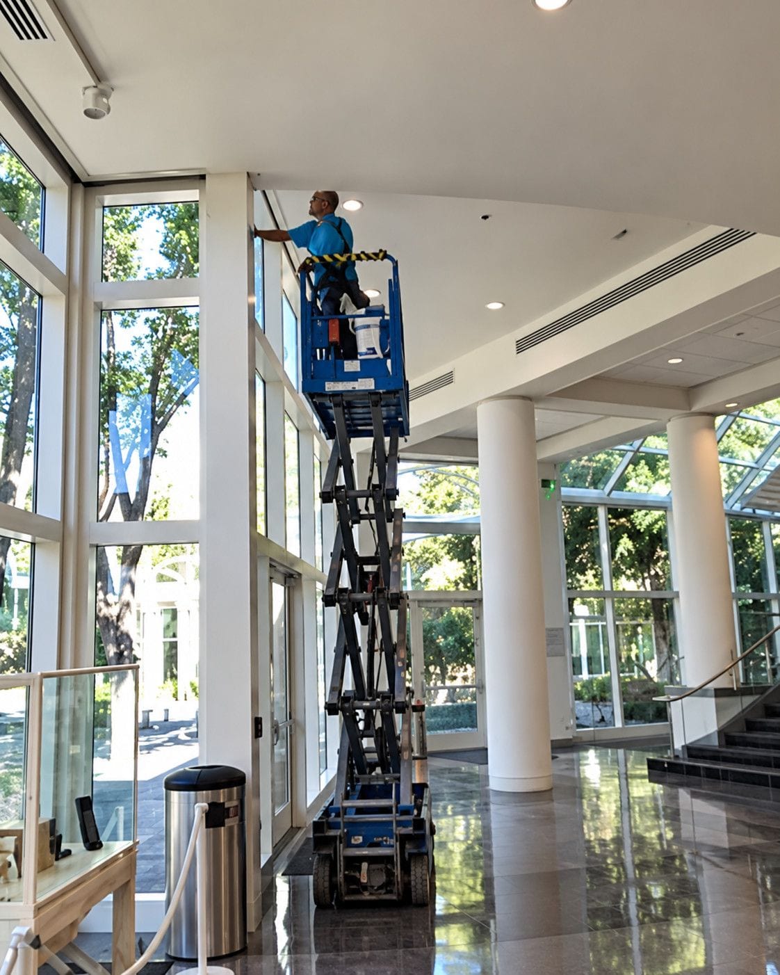 Technician on a scissor lift cleaning tall interior windows in a commercial atrium
