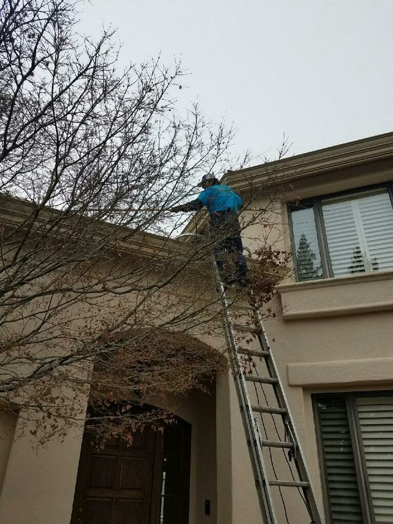 Technician on a ladder cleaning the gutters of a second-story home