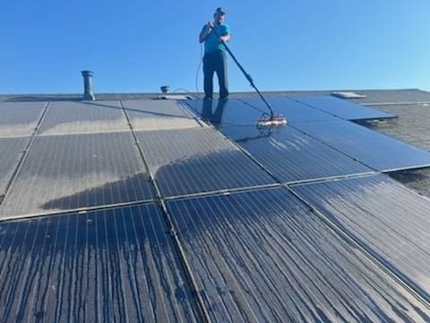 Technician using a long-handled brush on a rooftop solar panel array