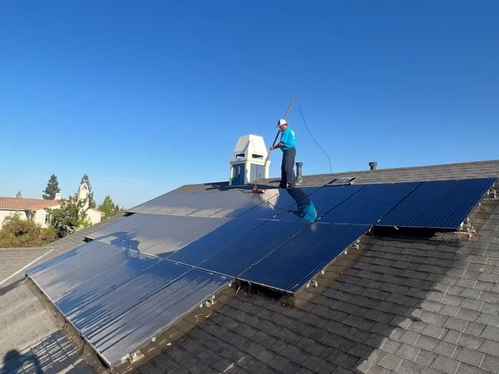 Technician using a long-handled brush to clean a residential rooftop solar panel array